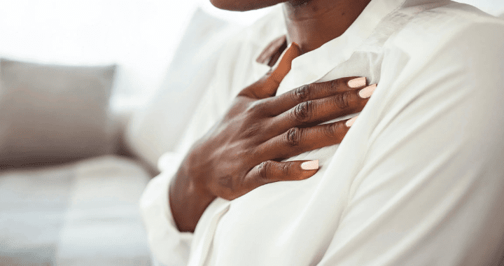 Image of Black woman practicing deep breathing touching chest sitting on a couch in the living room at home. Representing therapy technique to manage anxiety with an Atlanta therapist.