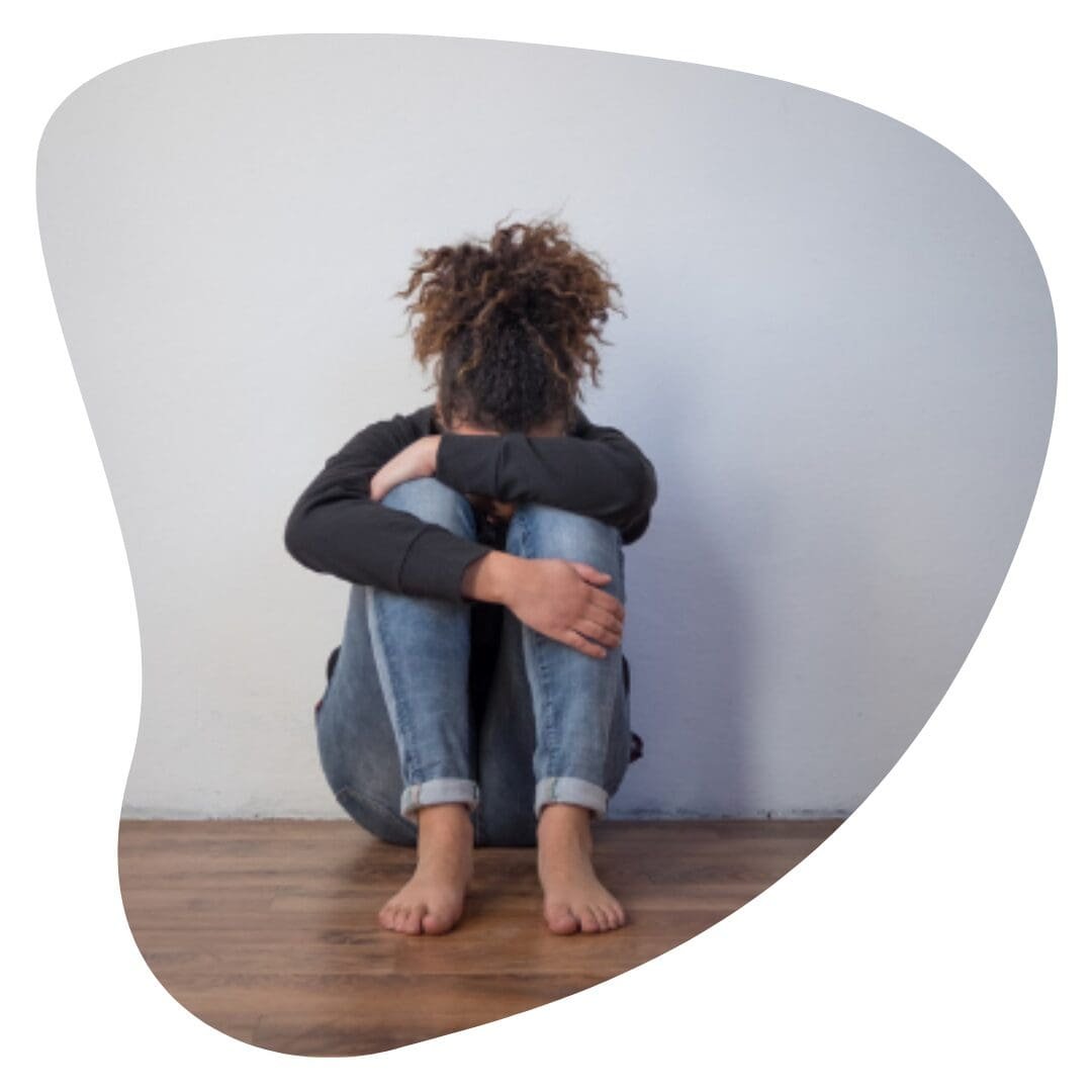 Sad and lonely black girl feeling depressed sitting on floor with head in lap and in need of trauma therapy