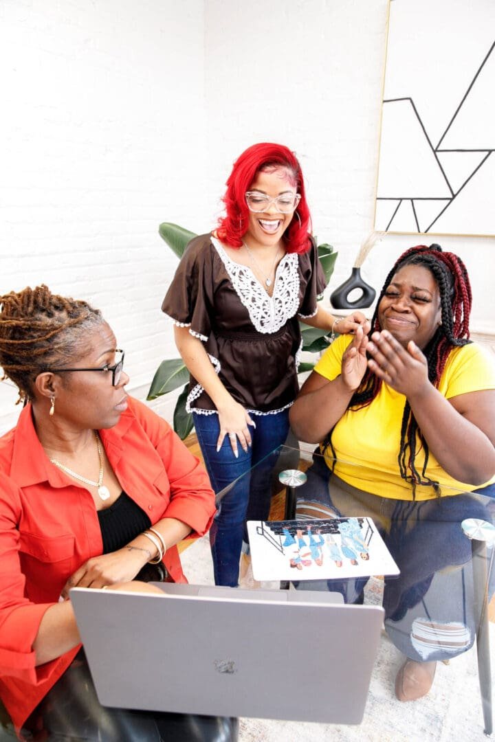 Three smiling colleagues gathered around a table, working together in a supportive community setting.