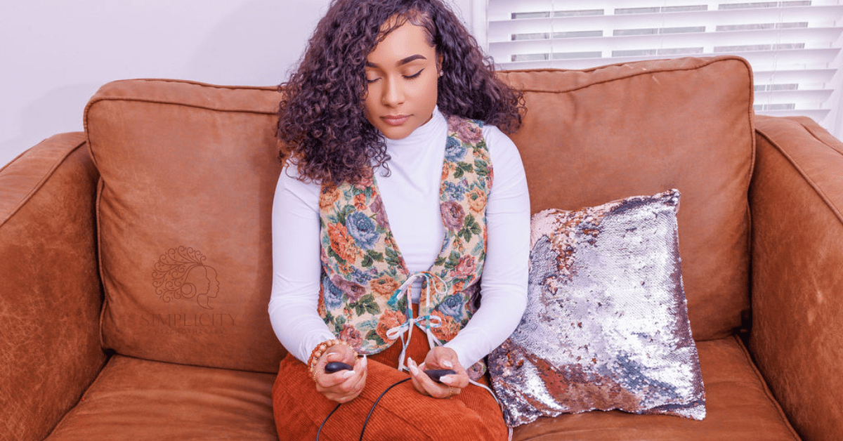 A woman seated on a couch with eyes closed while holding grounding tools in her hands, practicing nervous system regulation and stress relief through therapy in Georgia (30097, 30005, 30075, 30004).