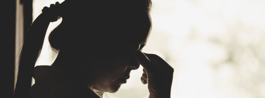 A woman sits in shadow, pinching the bridge of her nose in frustration and exhaustion, reflecting the emotional toll of high-functioning ADHD.