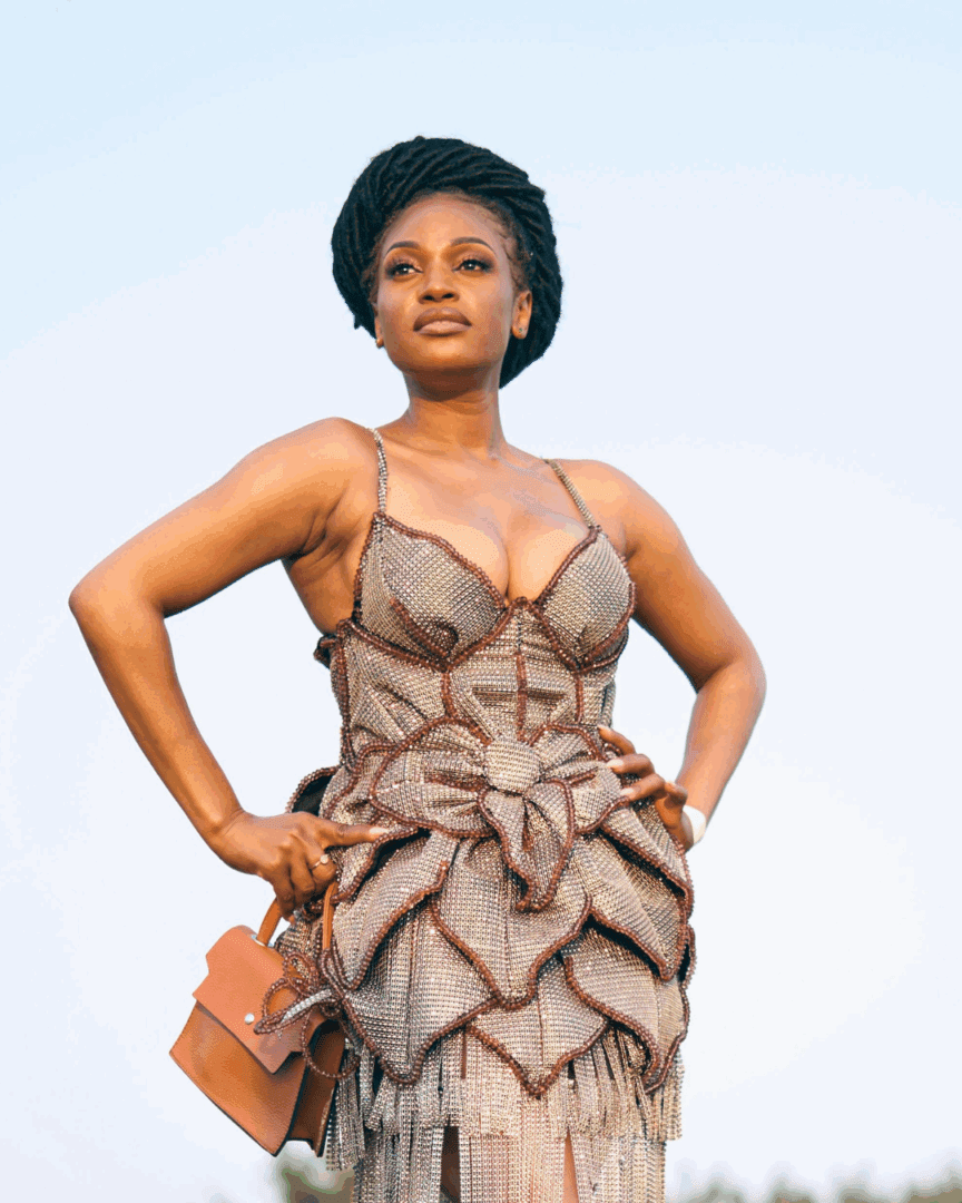 A Black woman in an ornate dress stands tall with hands on her hips, gazing upward with a self-confident presence, supported by therapy services for anxiety and balance.