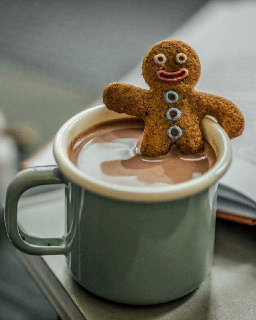A gingerbread cookie rests on the rim of a mug of hot chocolate, portraying the mix of comfort and quiet heaviness tied to holiday grief.