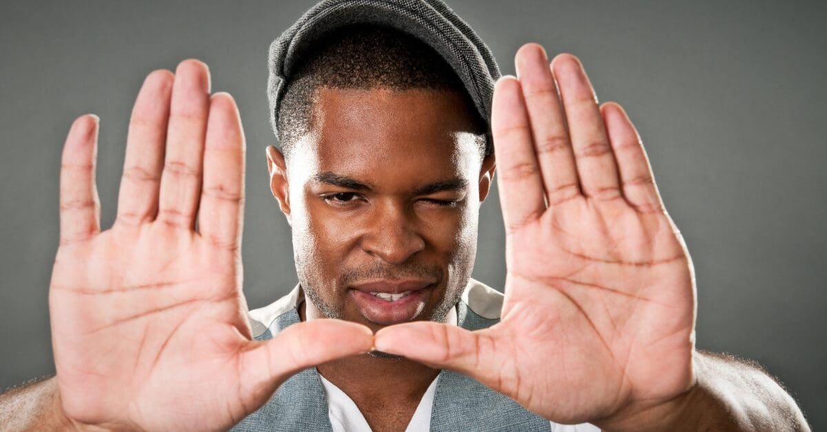 A man frames a rectangle with his hands while looking through it and winking, symbolizing focus, direction, and the intentional clarity behind values based goals.